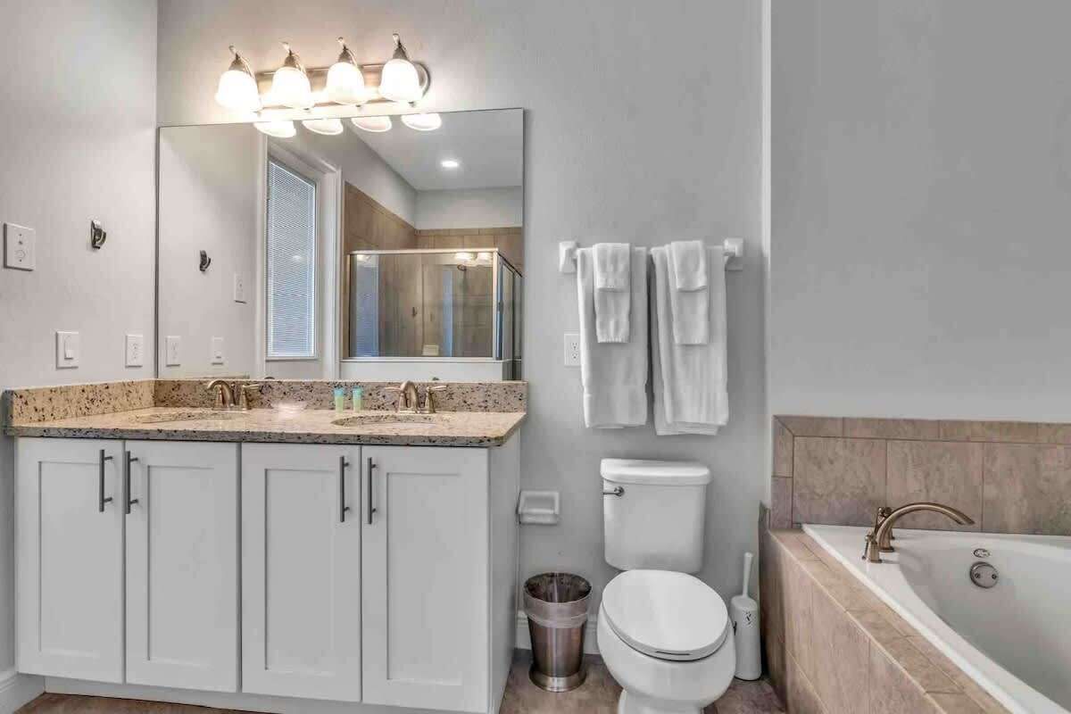 A bathroom with a large mirror, a sink, a toilet, and a bathtub.