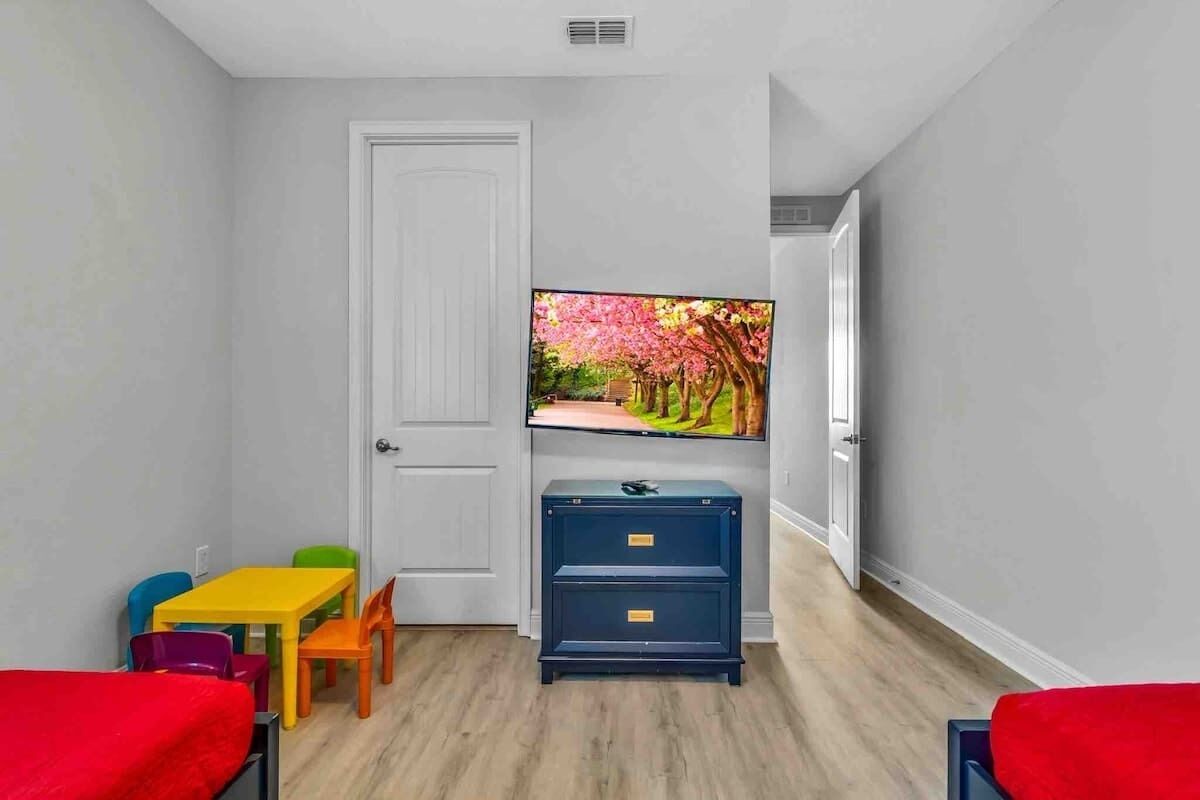 A room with a television, a door, a small table with chairs, and a bed.