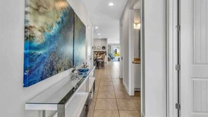 Une cuisine moderne avec un îlot central, un coin repas avec des chaises et un couloir menant à une porte.