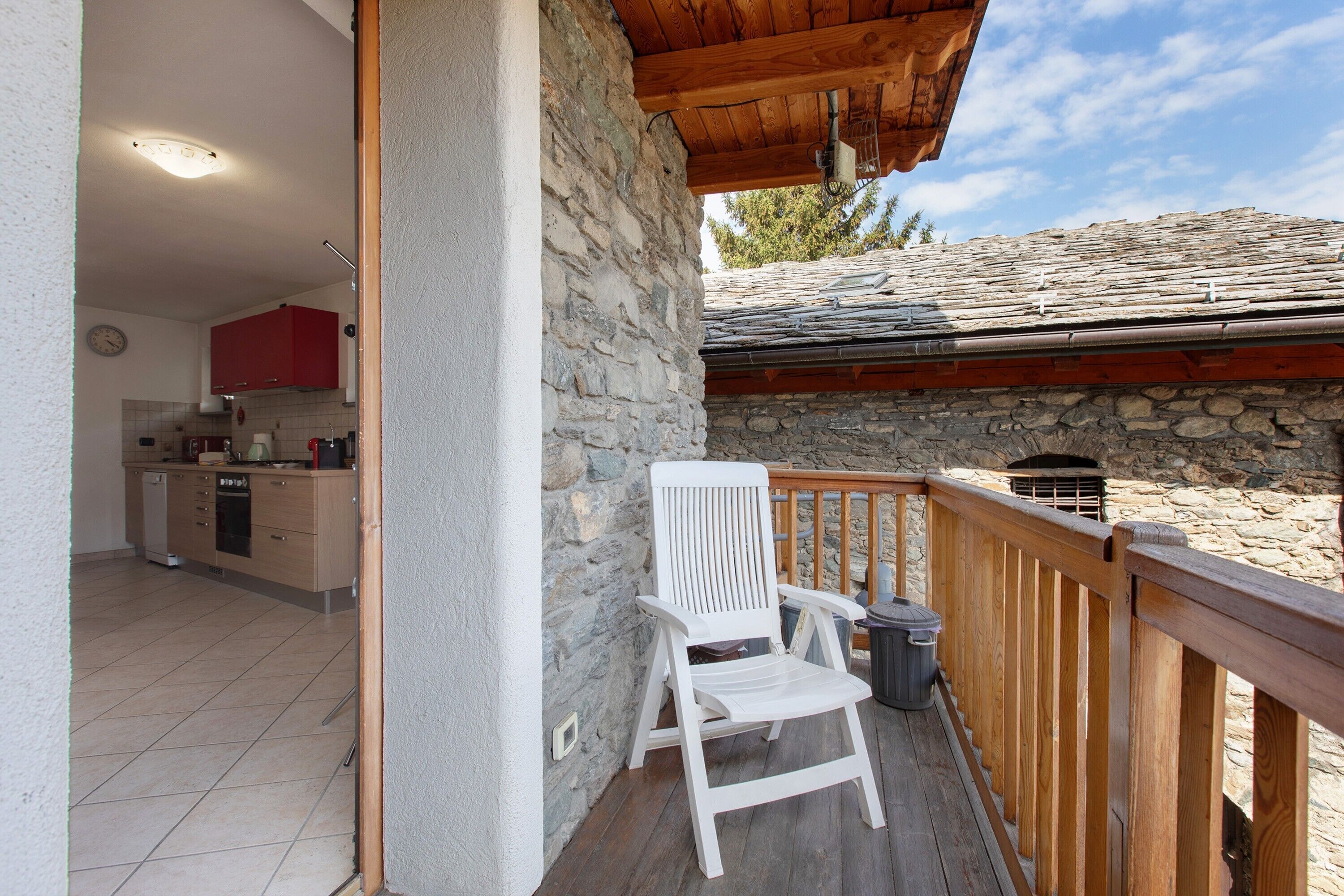 Une terrasse en bois avec une chaise blanche, un mur en pierre et une cuisine en arrière-plan.