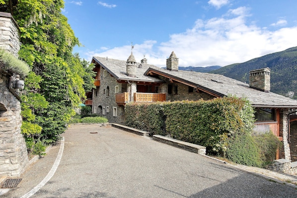 A stone building with a balcony, a stone wall, and a clear sky.