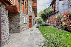 A stone building with wooden balconies and a stone pathway leading to a green area.
