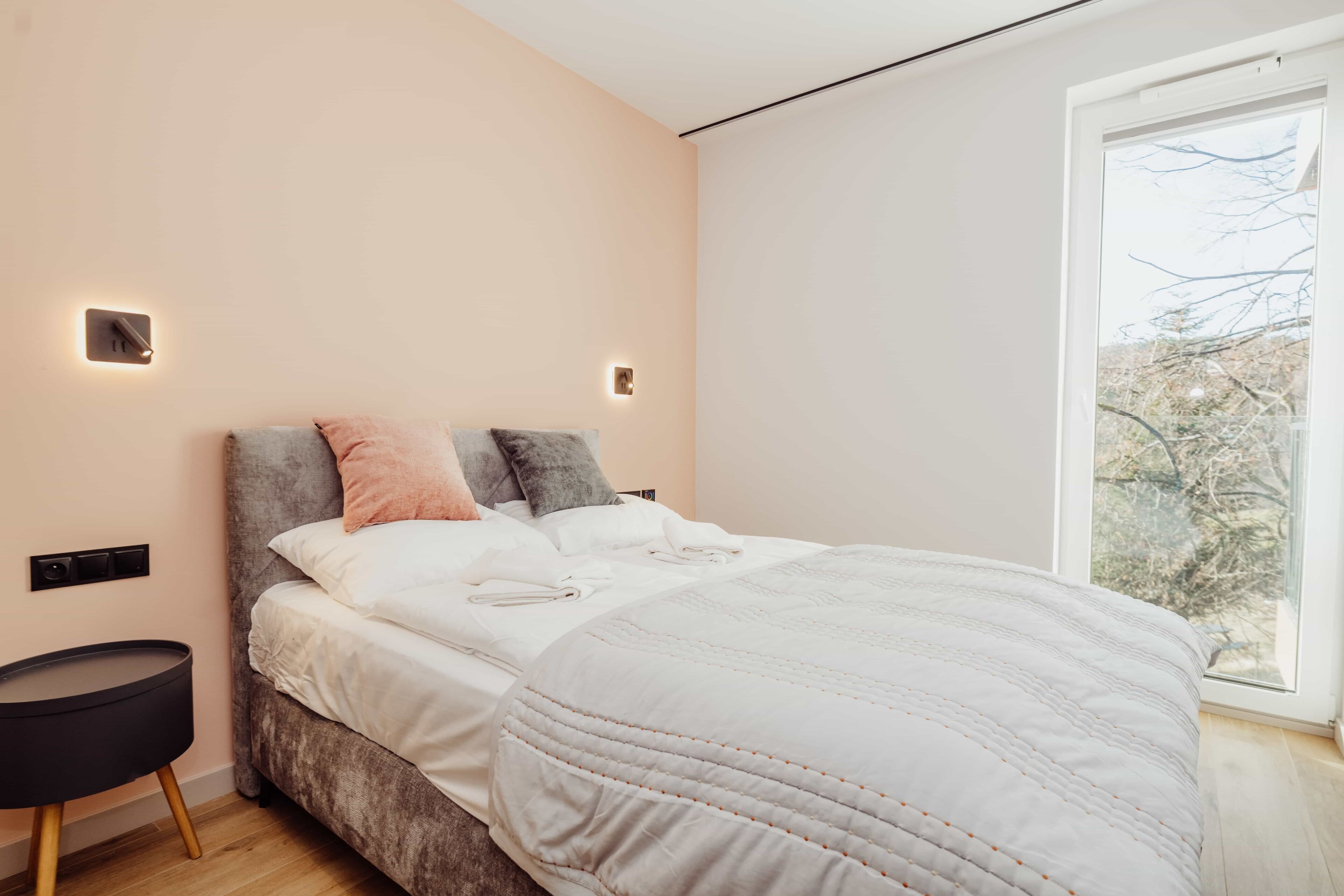 A modern bedroom with a large bed, bedside tables, and a window with a view.