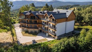 Un immeuble en bois à plusieurs étages, doté de balcons, entouré de verdure et avec des montagnes en arrière-plan.