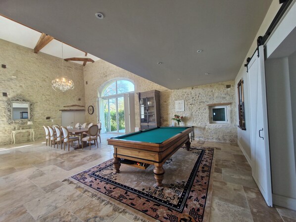 A spacious room with a pool table, a dining area, and a large window providing natural light.