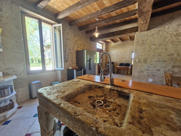 Une cuisine rustique avec un grand évier en pierre, des poutres en bois et une vue sur l’extérieur.