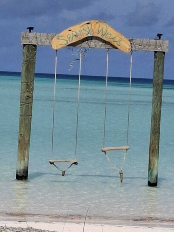 Eine Holzwentil-Anlage mit einem Schild, auf dem 'Spanish Wells' steht, vor dem Hintergrund von klarem, blauem Wasser und einem Strand.