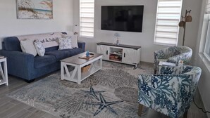 Una sala de estar con sofá, mesa de centro, televisor y sillón estampado.