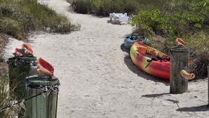 Un camino de arena que lleva al océano, con kayaks y una tabla de remo.