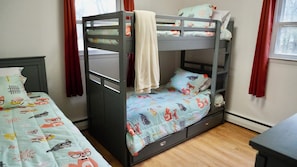 Un lit superposé avec un lit inférieur, un lit simple avec une couvre-lit à motifs et une petite commode.