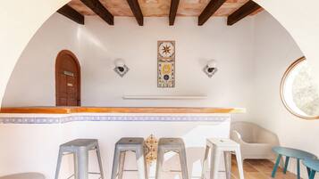 Un techo abovedado con vigas de madera, una zona de bar con taburetes, una puerta y apliques de luz en la pared.