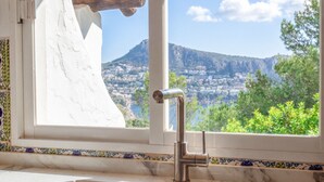A bathroom with a sink, a window with a view of a mountainous landscape, and a decorative tile border.