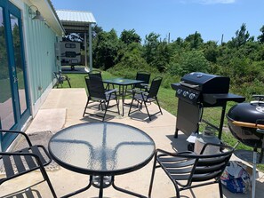 Une terrasse extérieure équipée d’un barbecue, de sièges et d’un espace abrité où se trouve un camping-car.