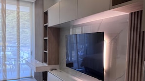 A modern living room with a large flat-screen TV, built-in shelving, and a sliding glass door leading to an outdoor area. - Edificio Delventto cerca a la Playa Cabo Tortuga (Santa Marta)