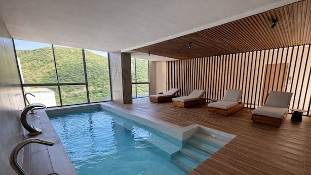 A modern indoor pool with clear views of a mountainous landscape, wooden flooring, and contemporary lounge chairs. - Edificio Delventto cerca a la Playa Cabo Tortuga (Santa Marta)