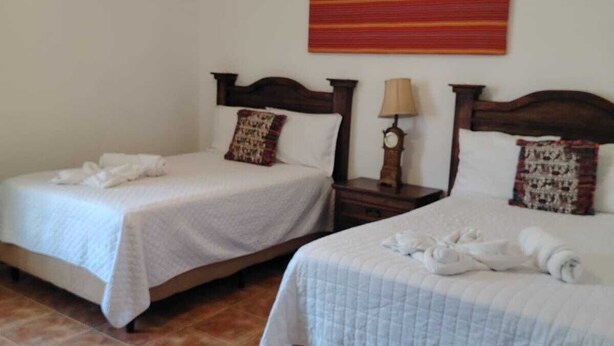 Two single beds with white linens, wooden headboards, and a red-striped wall hanging. - Alcázar de San Bartolo (Antigua Guatemala)