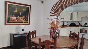 Ein Essbereich mit einem runden Holztisch und Stühlen, einem Bild an der Wand und einer Küche im Hintergrund.