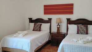 Ein Zimmer mit zwei Betten, einem Nachttisch mit Lampe, einer Deckenleuchte und einem Wandbehang mit roten Streifen.