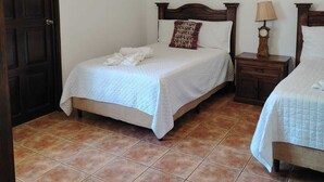 Ein Schlafzimmer mit zwei Betten, einer Holztür, einem Fliesenboden, einer Deckenleuchte und einer Wandlampe.