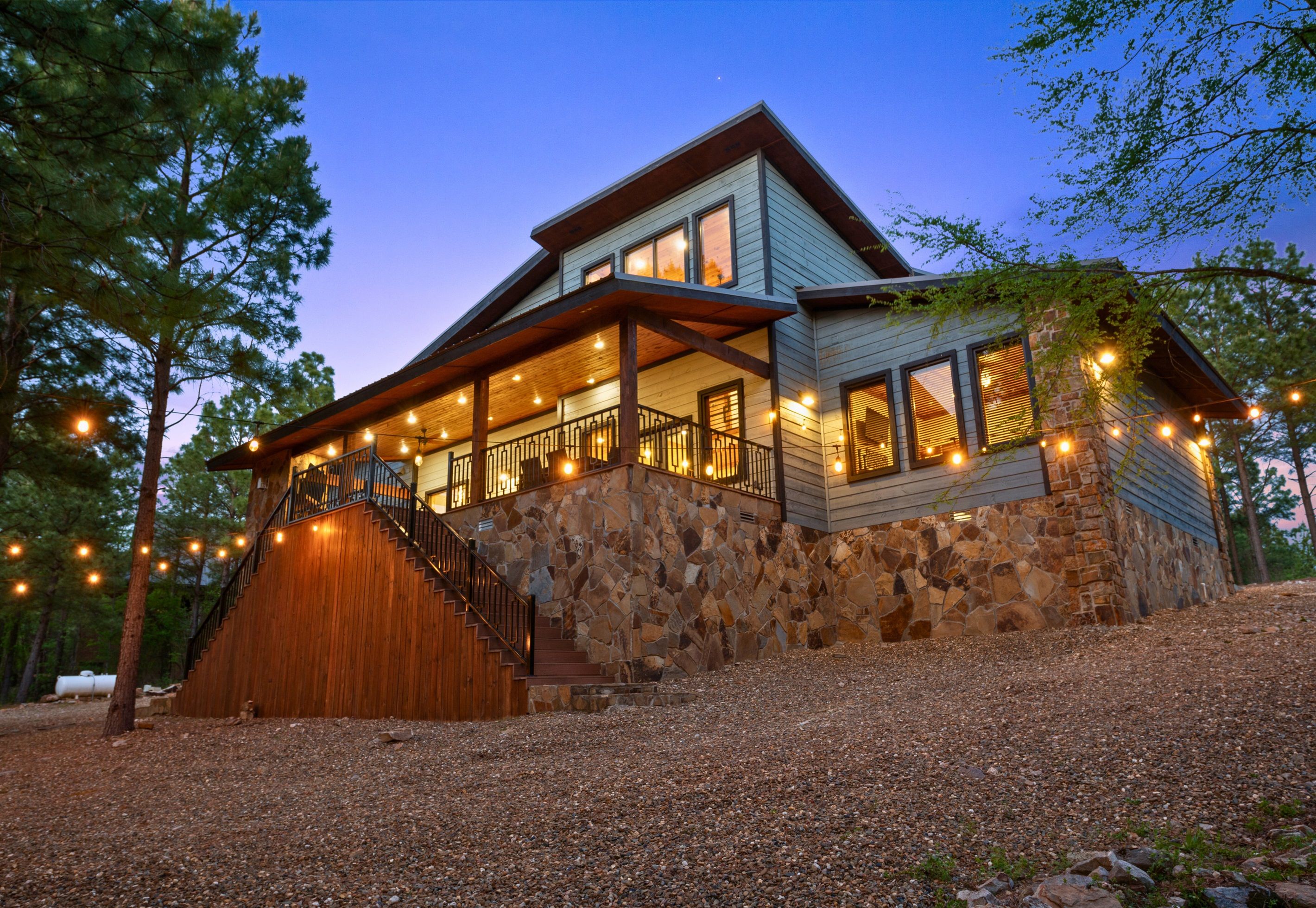 A two-story house with a stone foundation, wooden exterior, and a covered front porch with string lights.