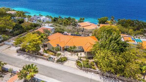 Uma área residencial costeira com casas de telhados laranja, rodeada por vegetação e vista clara do oceano.