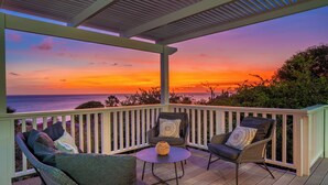 Uma área de estar coberta ao ar livre com vista para o pôr do sol sobre o oceano.