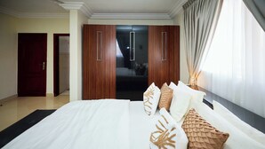 A hotel room with a large bed, wooden wardrobe, and a view of the city. - Willows Court (Accra)
