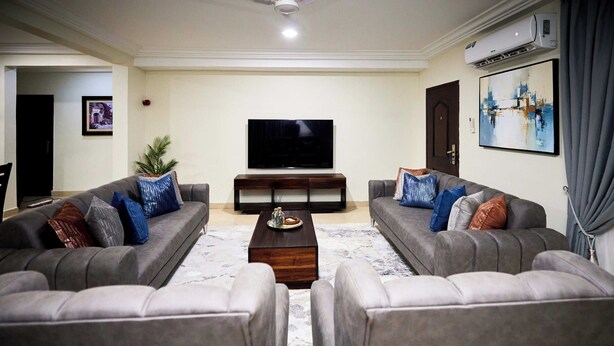 A living room with two grey sofas, a coffee table, a flat-screen TV, and a painting on the wall. - Willows Court (Accra)