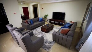 A living room with a sofa set, a coffee table, a television, and a clock on the wall. - Willows Court (Accra)