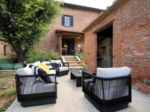 Un espace extérieur aménagé avec des meubles en osier, un bâtiment en briques en arrière-plan et un barbecue à l’extérieur.