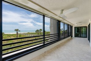 A balcony with a view of the beach and ocean, large windows, and a ceiling fan. - Gulfside Place 101: Beachfront Bliss in Sanibel! (Sanibel)