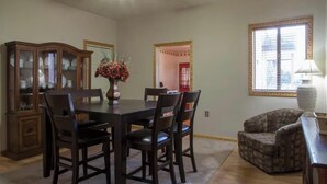 A dining area with a wooden table and chairs, a cabinet with glass doors, a vase with flowers, a patterned armchair, and a window with blinds. - NFL Draft week 3 Bedroom Bloomfield 10 minutes to Acrisure 3 parking spaces (Pittsburgh)