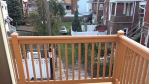 A wooden deck with a railing, a view of a residential street, and a clear sky. - NFL Draft week 3 Bedroom Bloomfield 10 minutes to Acrisure 3 parking spaces (Pittsburgh)