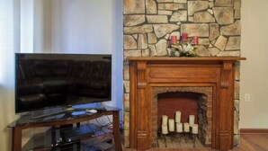 A living room with a stone fireplace, a television on a stand, and a decorative arrangement on the mantel. - NFL Draft week 3 Bedroom Bloomfield 10 minutes to Acrisure 3 parking spaces (Pittsburgh)