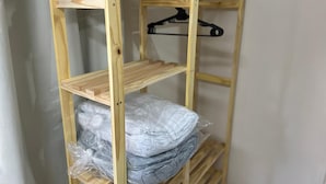 A wooden shelf unit with multiple shelves, some holding items, and a black hanger on one of the shelves. - Aeroconforto Residential - Near the Airport and Factories in Tarumã - Room 2 (Manaus)