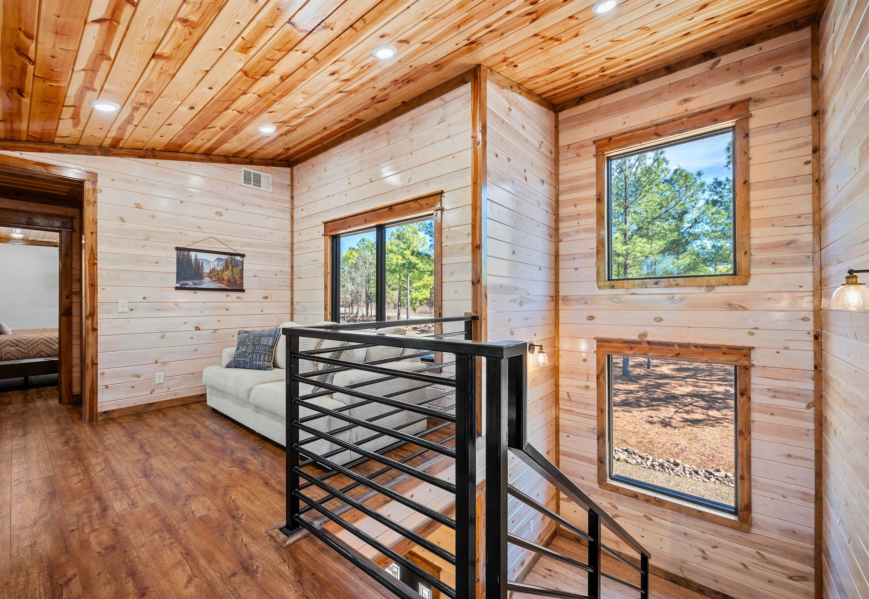 L’intérieur d’un chalet en bois comprend un escalier, un canapé blanc et de grandes fenêtres donnant sur la forêt.