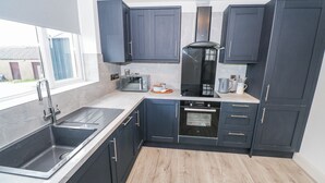 Een moderne keuken met donkere kastjes, een roestvrijstalen spoelbak, een inbouwoven en een raam dat voor natuurlijk licht zorgt.