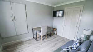 Een kamer met een bed, een bureau, een stoel, een aan de muur bevestigde televisie en een deur.