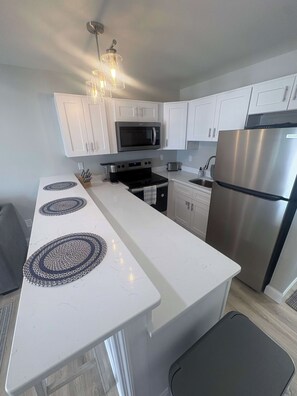 A modern kitchen with white cabinetry, stainless steel appliances, and a central island with decorative mats. - Cape May Harbor Getaway with Kayaks & Bikes (Cape May)