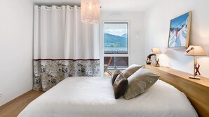 Une chambre à coucher avec un lit, une lampe suspendue, une fenêtre donnant sur un beau paysage et un tableau au mur.