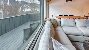En moderne stue med et stort vindue, træloft og en sofa med puder.
