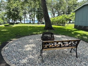 A bench in a gravel area with a tree and a building in the background.
