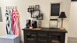 Eine Küchenzeile mit einer Kaffeestation, einem Schrank mit Schubladen und einer Tafel mit einer Willkommensbotschaft.