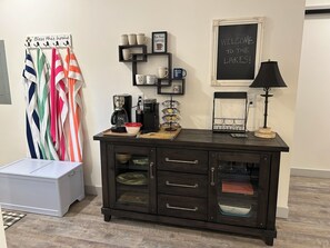 A kitchen area with a coffee station, a cabinet with drawers, and a chalkboard with a welcome message.