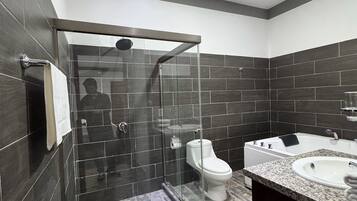 Un baño moderno con ducha envuelta en cristal, inodoro y tocador con lavabo.
