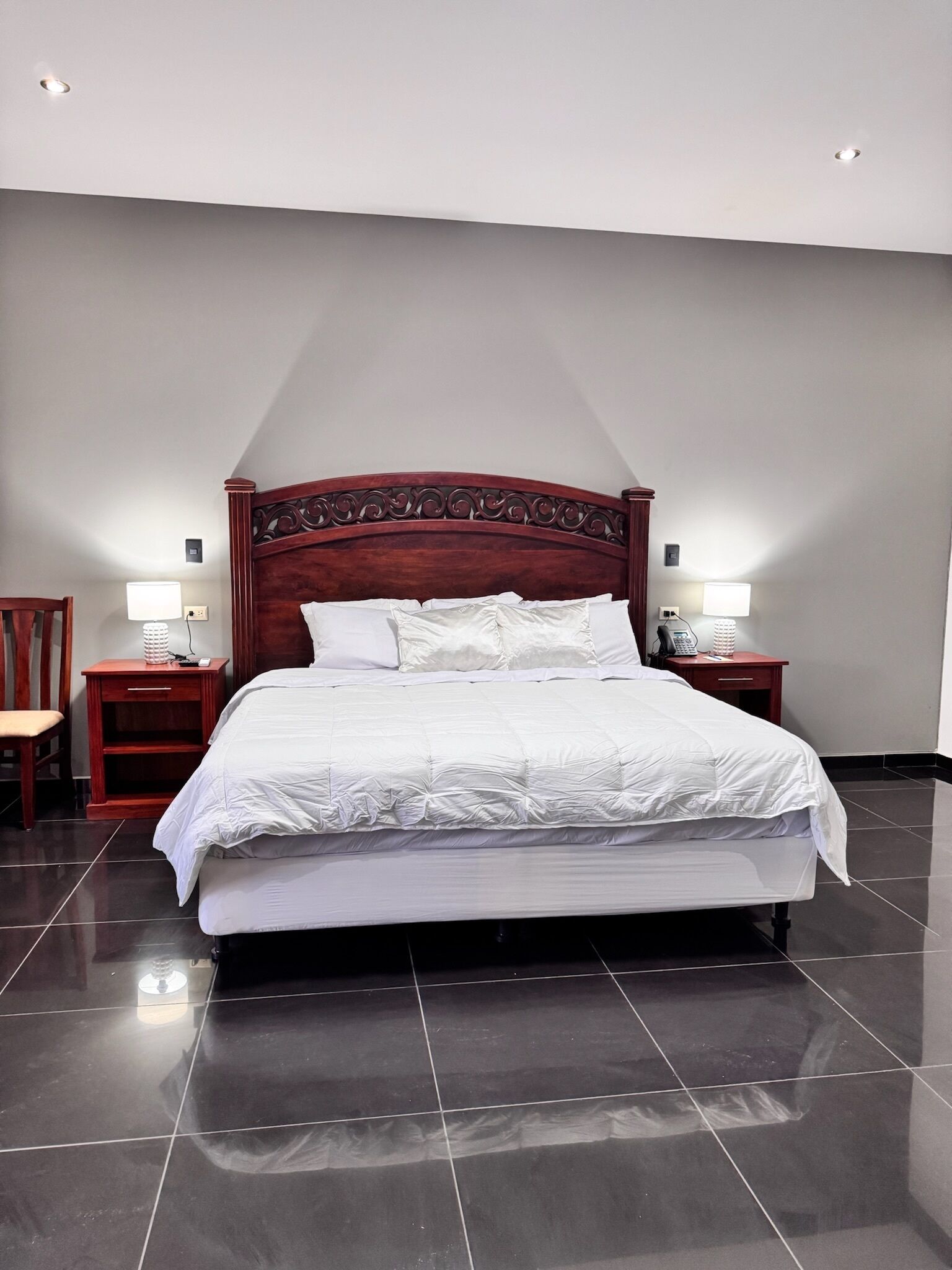 A neatly made bed with a wooden headboard, two bedside tables with lamps, and a chair.