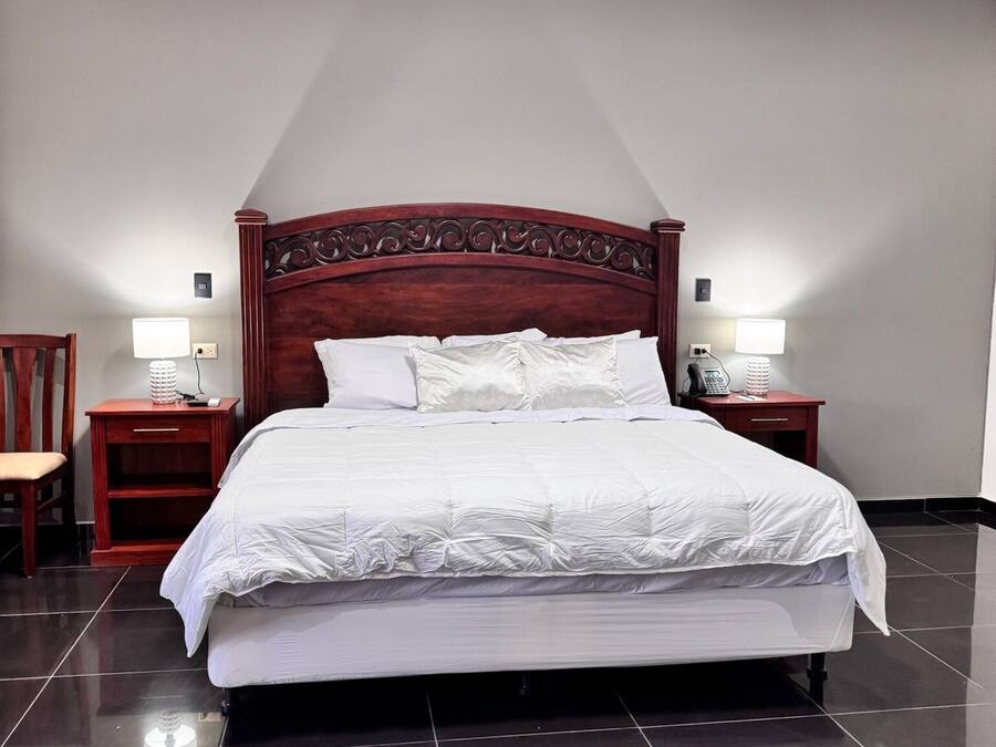 A neatly made bed with a wooden headboard, two bedside tables with lamps, and a chair.