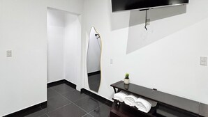 Une salle de bain moderne avec un grand miroir, un téléviseur à écran plat fixé au mur et un meuble-lavabo en bois foncé doté d’un porte-serviettes.