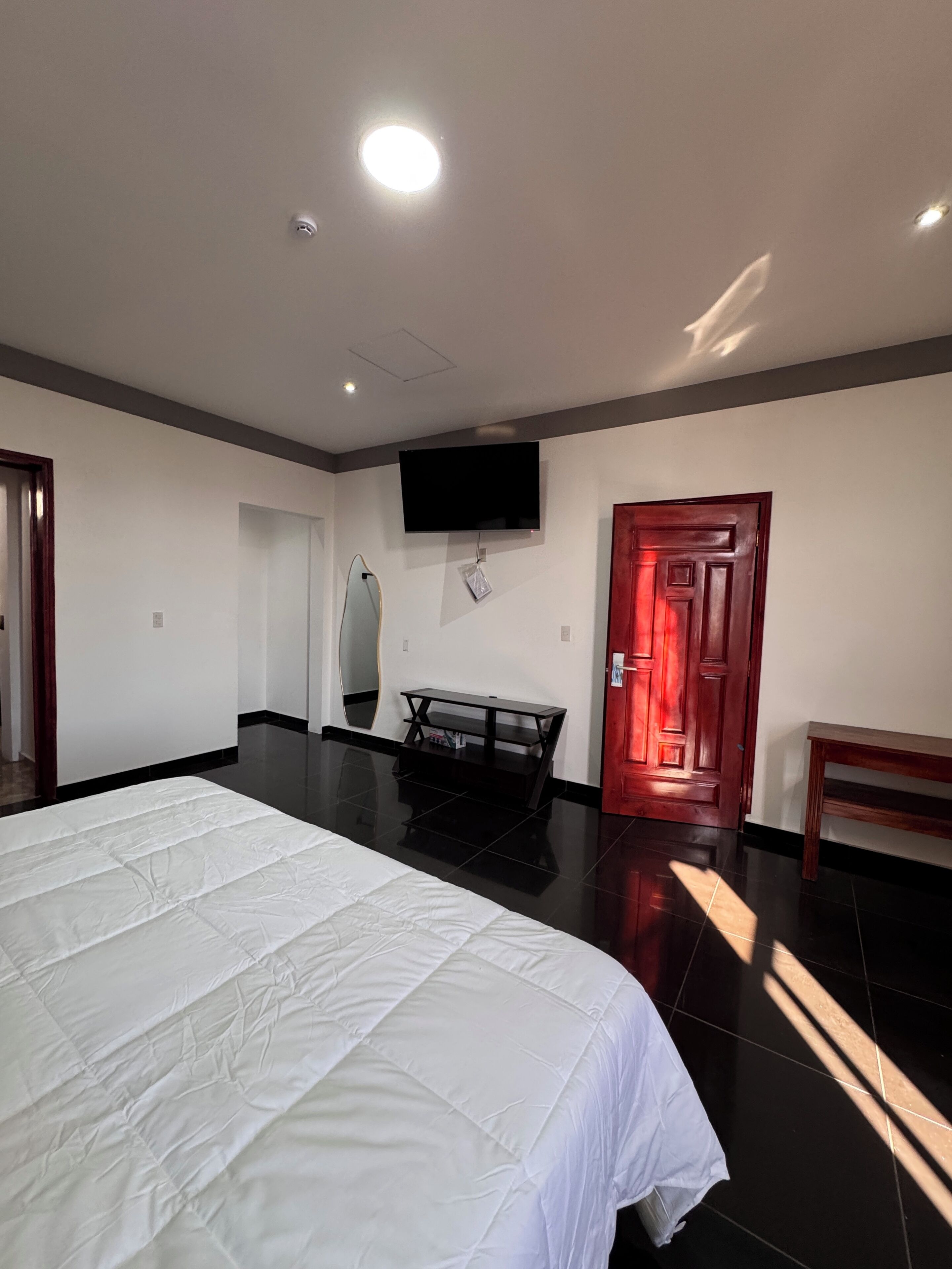 Une chambre d’hôtel avec un grand lit, un téléviseur à écran plat fixé au mur, une petite table et une porte dotée d’un cadre rouge.