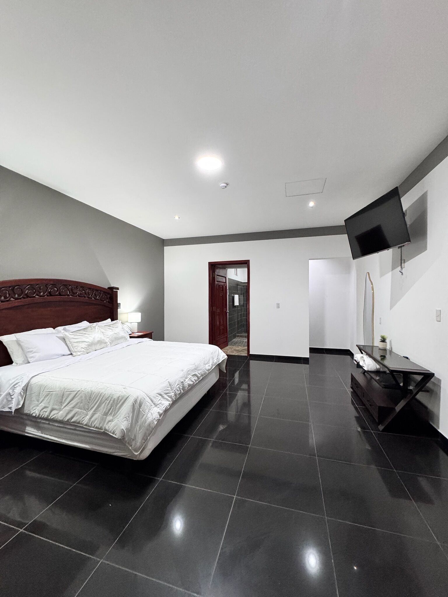 Un dormitorio moderno con una cama grande, un televisor de pantalla plana montado en la pared y un cabecero de madera oscura.